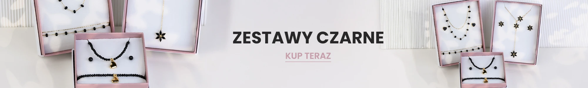 Zestawy czarnej biżuterii w ozdobnych pudełkach – naszyjniki, kolczyki i bransoletki z czarnymi koralikami i złotymi elementami. Napis: Zestawy czarne. Przycisk: Kup teraz.